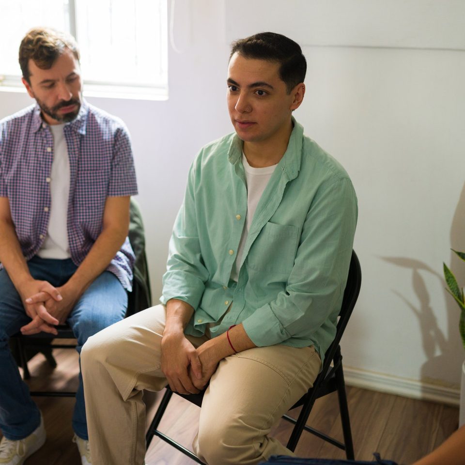 Two men sitting in a circle during a group meeting, listening