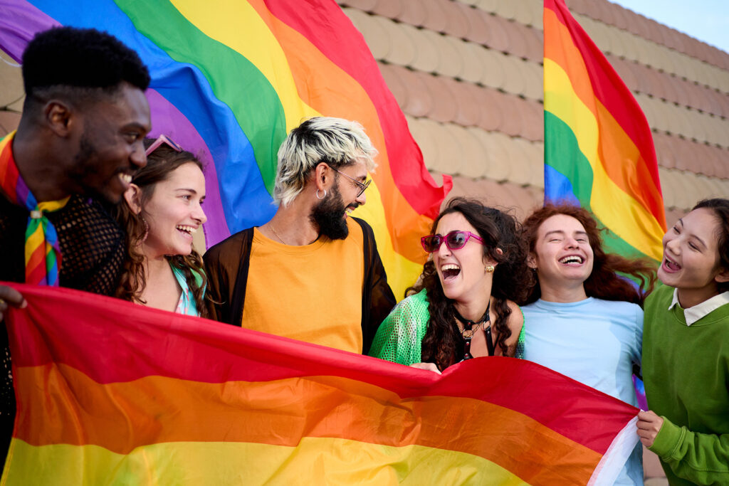 A group of young friends laughing and hugging outdoors on a Pride day